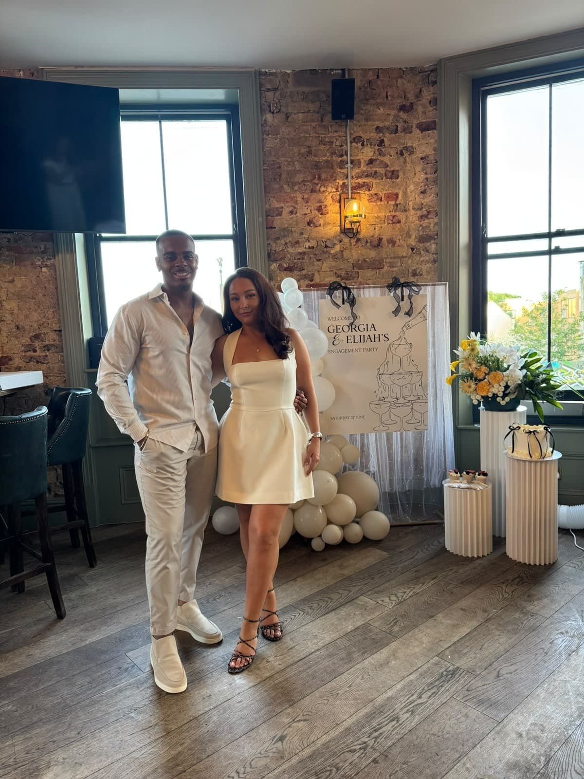 Georgia and Elijah at a party, in front of a sign with their names